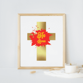 Gold cross with red paint splash with gold font that says "He's Alive"