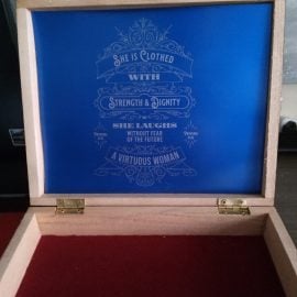 "Repurposed wooden cigar box decorated with a graphic design element inspired by Proverbs 31, featuring elegant script and symbolic illustrations representing strength, wisdom, and virtue."